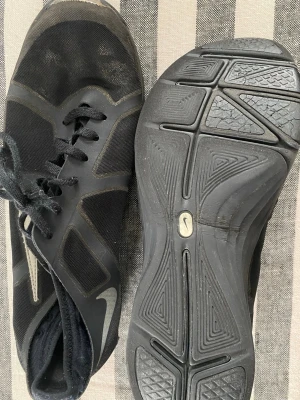 Svarta Nike LunarLon sneakers - Snygga svarta inne-träningsskor från Nike med LunarLon-sula för extra komfort. Skorna har en låg profil, mesh- och syntetmaterial samt klassisk snörning. Swoosh-logga på sidan och diskreta detaljer i grått. Har endast använts inne på gym.