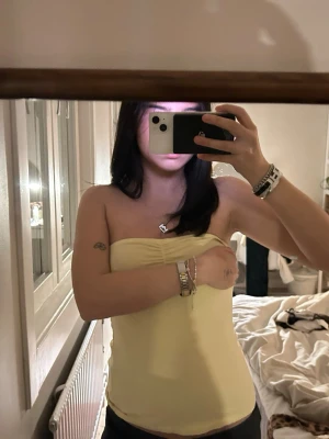 Gul bandeau tubtopp - Snygg ljusgul bandeau tubtopp i mjukt material. Perfekt för varma dagar och enkel att styla med olika accessoarer. Toppen är axelbandslös och har en tight passform som sitter på plats. Skiy snygg för sommarennn