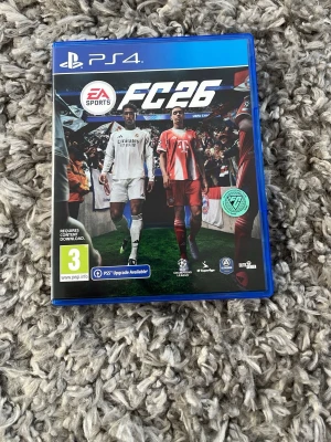EA Sports FC 26 till PS4 - Säljer spelet EA Sports FC 26 till PlayStation 4. Spelet kommer i ett blått plastfodral med omslag och skiva. Omslaget visar fotbollsspelare i vita och röda matchställ på en fotbollsarena. Perfekt för dig som gillar sportspel och fotboll.