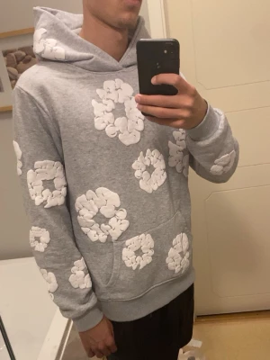 Grå hoodie från Denim Tears med blommor - Säljer en grå hoodie från Denim Tears med vita, upphöjda blommönster över hela tröjan. Hoodien har en stor huva och magficka, samt ribbade muddar vid ärmslut och nederkant. Perfekt för dig som gillar streetwear och unika prints. Pris går att diskutera 