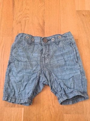 Jeansshorts med knappar - Snygga jeansshorts med flera knappar i midjan och klassiska fickor fram från Lindex i storlek 68. Perfekta för varma dagar och har en avslappnad passform. Stilen är enkel och tidlös, passar till det mesta i garderoben.