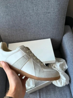 Maison margiela gats 43 - Stilrena sneakers i vitt och beige med ovandel i läder och mocka, samt klassisk gummisula. Snygg minimalistisk design med neutrala färger och diskreta detaljer. Perfekta för dig som gillar en clean look och vill ha något som funkar till det mesta.