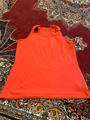 Röd ärmlös linnetopp - Snygg röd linnetopp i enkel och stilren design. Toppen är ärmlös med rund halsringning och tillverkad i mjuk bomull, perfekt för varma dagar eller lager på lager. Passar dig som gillar en clean och sportig look.