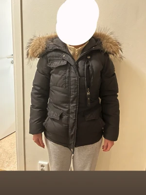 Svart pufferjacka med fuskpäls - Snygg svart pufferjacka med Luva och fuskpäls. Jackan har dragkedja, flera fickor med lock och en bröstficka med dragkedja. Perfekt för kalla dagar och har en klassisk, tidlös look. Jackan är vadderad och har en figurnära passform. Möts hällre upp, vi finns i stockholm/södertälje.