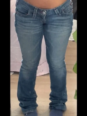 Blå bootcut jeans med låg midja - Säljer ett par true religion blå bootcut jeans med låg midja. Jeansen har slitningar och en lätt tvättad look, perfekta till sneakers eller boots. Säljer då dom är försmå. OBS! Inte mina bilder, kan skicka egna bilder om man vill det. Kan kanske tänka mig gå ner i pris lite 