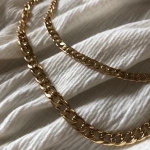 Halskedja i två rader  - Guldfärgad halskedja i två rader, osäker på material. Reglerbar längs med klolås.