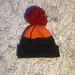 Bollmössa - Svart/orange/röd bollmössa i one size. Håller värmen, perfekt till höst/vintern. Toffs som är påsydd.