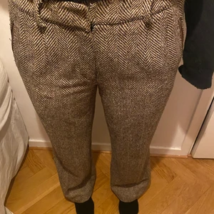 Byxor i brunt fiskbensmönster  - Coola brallor, inköpta secondhand! Låg midjade byxor som sitter snyggt storlek mellan M o S beroende på hur man vill att de ska sitta.