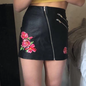 Fin skinnskallar med blommor  - En fin kjol i skinn imitation med broderade blommor. Kjolen är aldirg använd men har dock tagit av lapparna. Priset kan diskuteras vid snabb affär  