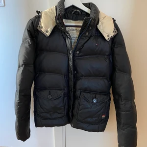 Tommy hilfiger jacka  - Väl använd dunjacka från Tommy hilfiger. Köpte denna för många år sedan och dunet har delat sig lite i armarna men tycker den har mer kvar att ge! Fin knytdetalj i ryggen. Det är storlek medium men skulle säga att den är mer som en small. 