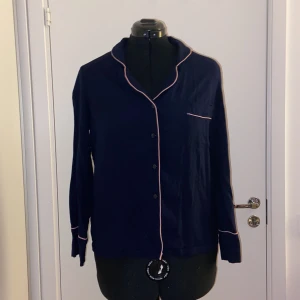 Avslappnad Marinblå Skjorta med Rosa Söm - Mörkblå skjorta i pyjamas stil med rosa detaljer och fricka på bröstet. Nyskick, använd 1 gång.