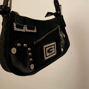 Real Gussaci handväska  - Detta är en märkesvöska i hela okej skick. Det saknas två stenar på framsidan och finns små märke på axelremmen vilket är förståligt för en äldre väska. Denna är cool att styla nu till 2000-tals mode men också till annat. Cool att ha i er collection och den ör defenitift TIMELESS!! 