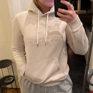 GANT hoodie  - Beige/krämvit med vita detaljer (tryck och snören). Storlek S