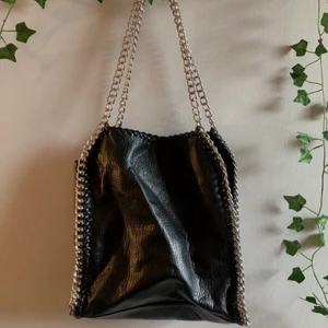 Tiamo väska i svart - Svart handväska från Tiamo med silvriga detaljer som påminner om Stella McCartney väskorna. Väskan är i extremt fint skick. Rymmer mycket och passar därför superbra att använda som skolväska då man får plats med dator, böcker plus mycket annat som är bra att ha med sig i vardagen. Stort plus att den har mindre fack och att man även kan stänga den med dragkedja. Köparen står för frakten! Detta är en intressekoll och säljer endast vid bra bud!😄