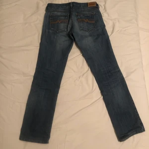 Lågmidjade jeans - Byxor i använt skick köpa second hand. Innerbenslängd 74cm. Midja ca 80cm. Längd från skrev till knappar 17cm. 