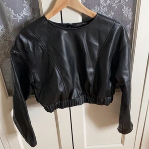 Cropped skinntröja (fuskskinn) - Skitsnygg topp i skönt och stretchigt material. Passade desvörre inte. Dragkeja på baksidan vid nacken. Storlek en passar 36/38.