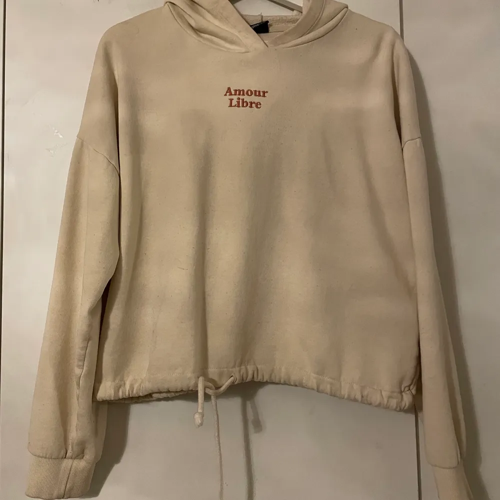 En beige hoodie med texten amoure libre på bröstet och den har även så att man kan knyta den i midjan. . Hoodies.