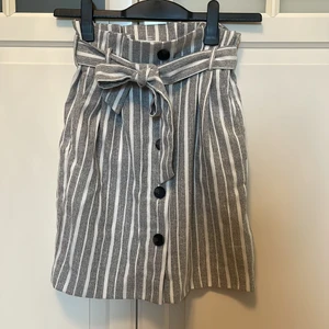 Randig kjol, högmidjad - Mycket bra skick, som ny! Stora fickor där fram och dragkedja som man knäpper på sidan. Avtagbart band som man knyter vid midjan.