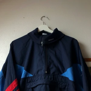 Vintage Vindjacka  - Svinball mörkblå vindjacka med röda och ljusblå detaljer. Den har en stor ficka på magen och hål för tummarna. Perfekt för att springa eller som vårjacka. Säljer då den inte riktigt är min stil. Väldigt fint skick