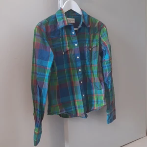 Skjorta - Rutig skjorta, fina färger, jättebra skick! Insvängd midja. Knäpps med tryckknappar som håller bra. Passar strl 34/36.