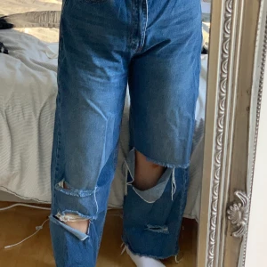 Baggy byxor med slitningar  - Baggy blåa byxor med slitningar vid knäna, hög midjade.