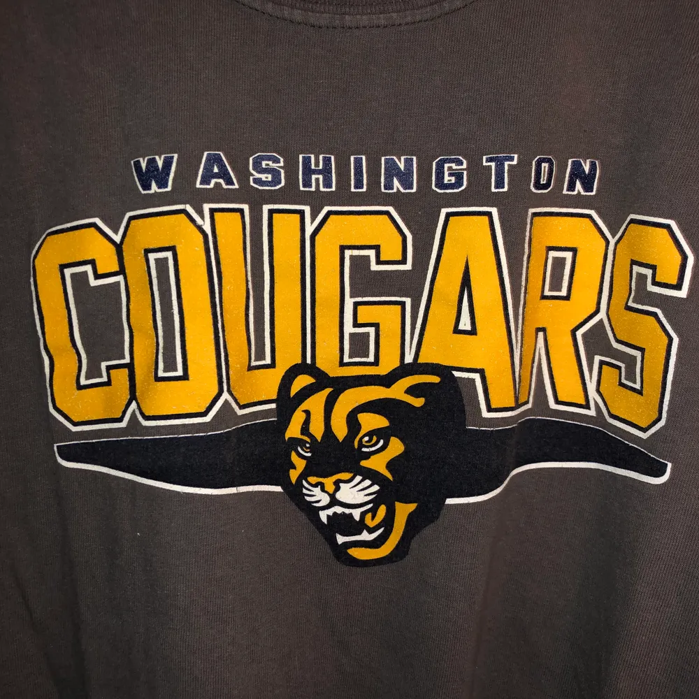 Mörkgrå T-Shirt med stort gult tryck på bröstet. Washington Cougars. Uppvikta ärmar. . T-shirts.