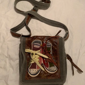 Retro axelremsväska  - Häftig axelremsväska med skomotiv! Inköpt second hand så är i använt skick. Möts i Stockholm & kan säljas direkt vid snabb affär 