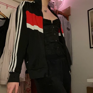 Adidas kofta - Mjuk och skön adidaskofta med hög krage. Den har  röda och vita ränder över bysten och klassiska tre streck längs båda ärmarna. Den är från herravdelningen men passar med lös fit på mig som vanligen bär M. Köparen står för frakt