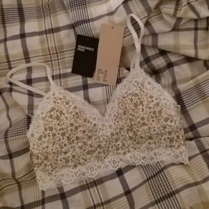 Blomig vit BH topp från H&M - Jätte fin blomig vit topp från H&M i strl 36, endast prövad en gång och har tvättats efter det. Ny pris: 150kr säljs pga för liten storlek. Kommer med pads i som går att ta ut.