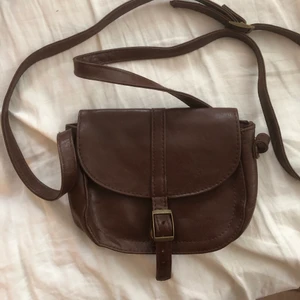 Brunt skinn axelremsväska  - Liten och söt axelremsväska i brunt skinn, ej äkta. Hel och ren! Går att justera banden. Frakt tillkommer. 