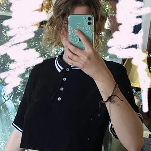 Croppad svart och vit t-shirt - En croppad t-shirt i svart färg och vita ränder. Den har krage och knappar och har endast använts ett fåtal gånger. Den är köpt från h&m och original priset var 200 tror jag.