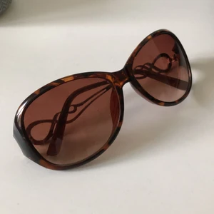 (GRATIS) Bruna solglasögon med gulddetaljer - Fina bruna bågar som är sparsamt använda. Dessa skickas med, utan kostnad, till den som köper något mer plagg från mig (kommer inom kort). I gott skick förutom; det saknas en strassen på högra sidan av bågen och lite lös på vänstra sidan (bör dock kunna åtgärdas med en liten skruvmejsel). 