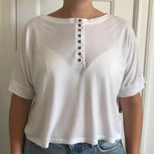 Vit T-shirt - Monki - En vit T-shirt med bruna små knappar som detalj framtill. Från Monki och i bra skick. Passar strl. M, L. 
