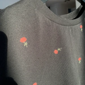 Svart t-shirt med blommor  - Svart T-shirt med röda rosor 🌹! Använd ett antal gånger men ändå i bra skick. Är lite kortare i modellen så skulle säga att den passar bäst på en XS.