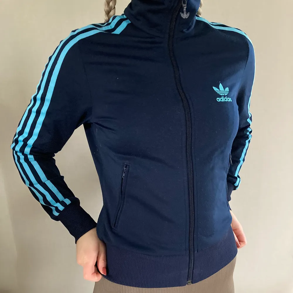 Marinblå ”track jacket” från adidas med turkosa/ljusblå detaljer. Hög krage och fickor. . Jackor.