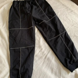 Svarta byxor m. Reflexdetaljer nyskick - Svarta byxor med reflexdetaljer i polyester. Åtstramning vid anklarna. Ötöver det lös passform. (helt oanvända). 