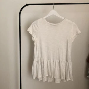 T-shirt med volang  - Vit T-shirt med volang detalj. Säljer för den inte kommer till användning längre. Skönt och tunt material, perfekt för varmt väder