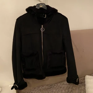 NA-KD jacka strl 38 svart - Jacka från NA-KD, fejk mocka med fluff armar (handled) och krage. Inga slitage, köpt 2019. Hela insidan är av likadant fluff som armar och krage i hela insidan. Dragkedja längs med framsidan, två fickor fram, spänne vid krage. Mysig helg och varm. Frakt exklusive pris