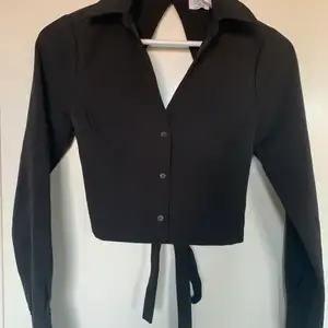 Jättesnygg svart croppad skjorta med öppen rygg ifrån na-kd x Hanna Schönbergs kollektion! Den är i storlek 32, jag har vanligtvis 34 och den passar mig men har tyvärr inte kommit till användning❣️ prislappen sitter kvar. Säljer den för 100kr🥰