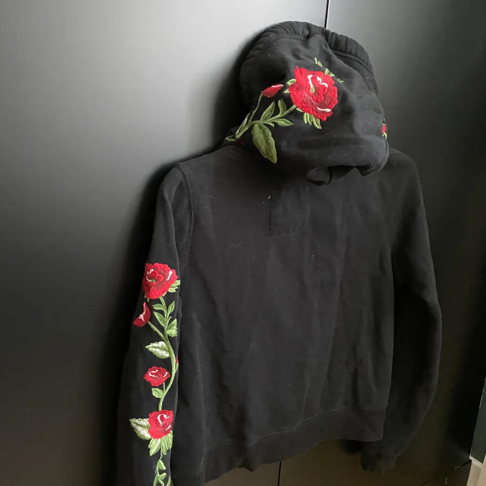 Har en hollister hoodie som är svart med röda rosor på. Rosorna går längst armarna och på luvan. Är i storlek S men är i kortare modell.. Tröjor & Koftor.