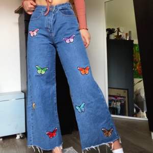 Ankellånga vida jeans med broderade fjärilar längs framsida ben och slitningar längs ned. Byxorna har både fram- och bakfickor och är i 100% bomull. Stl. S (sitter ungefär som en stl. 38)