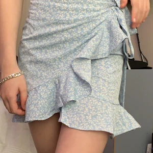 Blå fin kjol med små blommor - Fin somrig blå kjol med små blommor. Den går att knyta om och justera vid midjan. Bra skick!