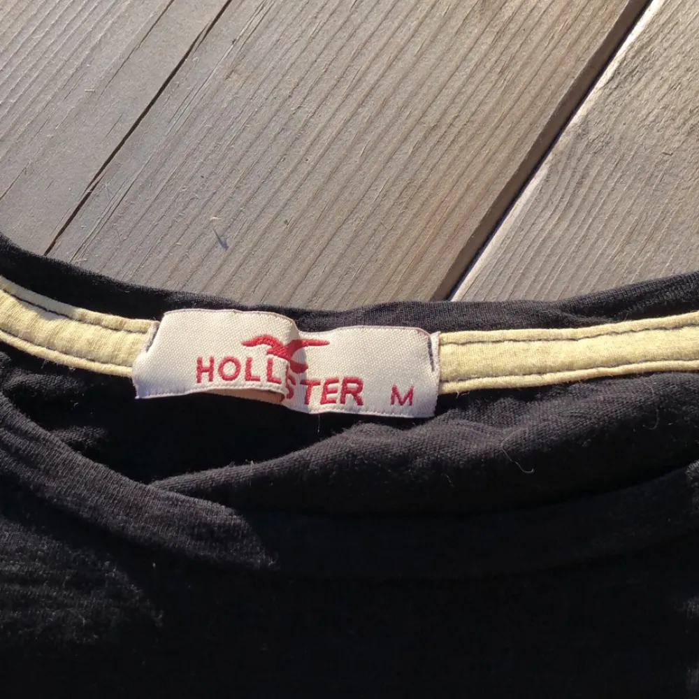 En svart rätt tajt t-shirt från Hollister. Rosa märke på bröstkorgen. Väl använd men i fint skick.. T-shirts.