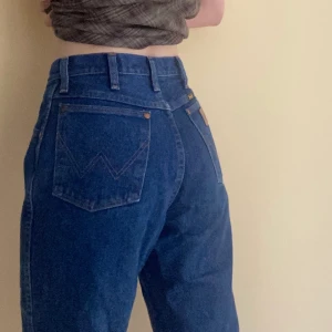 Högmidjade Mörkblå Raka Wrangler Jeans - Högmidjade mörkblå raka wranglerjeans. Midjemått: 75 cm, Längd: 95 cm. OBS - katt ingår ej :))