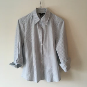 Stretchig blå- och vitrandiga skjorta från tidiga 00-talet - Snygg stretchskjorta med uppvikt ärm och låg knäppning. Väldigt 00-talig :)