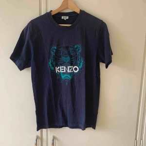  - Cirka 3 år gammal mörkblå t-shirt från Kenzo i storlek M, köpt på Kenzos hemsida. Har ett litet hål nere vid kanten och därmed kan priset diskuteras.