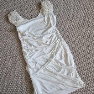 Klänning  - Kort vit draperad klänning med axelvaddar och pärlor på axlarna. Aldrig använd. 