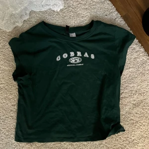 Tröja - En grön kortare tröja med tryck där det står cobras och en liten bild på en orm från H&M använd Max 2 gånger. Storlek M. Kan säljas billigare vid snabb affär 💚🫶🏼