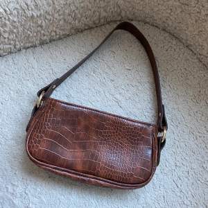 Snygg handväska från Asos. Aldrig använd så det finns inga anmärkningar. Väskan är i brunt fake skinn och är 13cm hög & 24 vm bred. 
