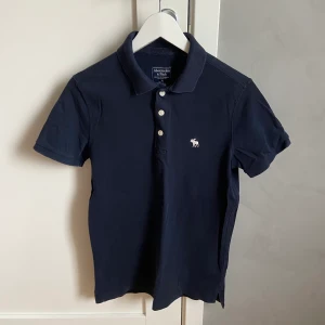 Piké från Abercrombie & Fitch - Pikétröja från Abercrombie & Fitch, storlek XS (passar unga barn/tonåringar), fin marinblå färg. Använd flertal gånger men i bra skick. 